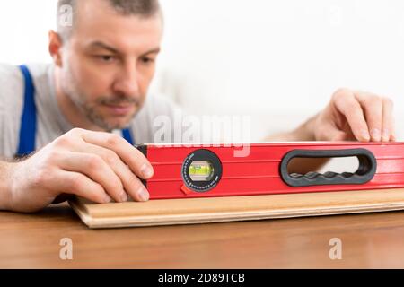 Carpenter Using Level Working With Wooden Board Making Shelf Indoors Stock Photo