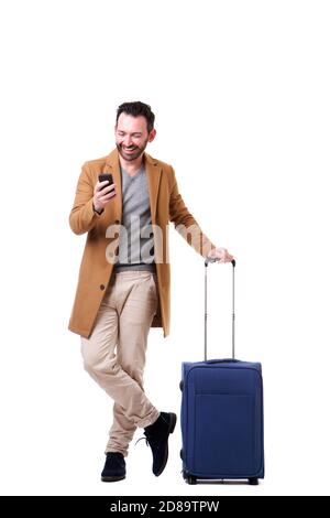 Full length portrait of male traveler standing with mobile phone and suitcase against white background Stock Photo