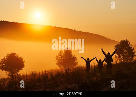 Beautiful fog in the morning. Silhouettes of three people - dad and two children against a beautiful golden sunrise. Hills in the Beskids, Poland. Stock Photo