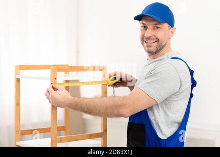 Carpenter Measuring Shelf Working Standing Indoor, Smiling To Camera Stock Photo