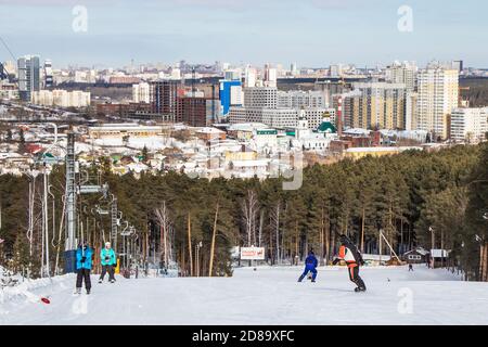 Yekaterinburg, Russia - February 26, 2019: People go skiing and snowboarding on the training slope of the sports complex on Uktus mountain. In the bac Stock Photo