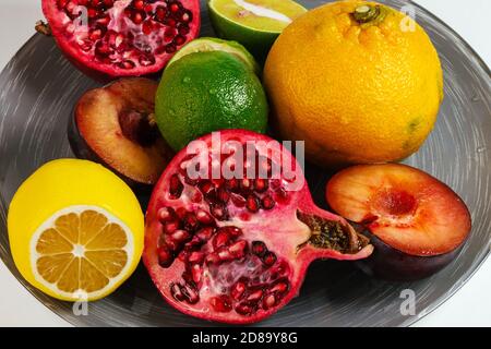 Mandarin, lime, lemon, pomegranate and plum on a gray dish isolated on white background. Fresh summer fruits composition. Upper view Stock Photo