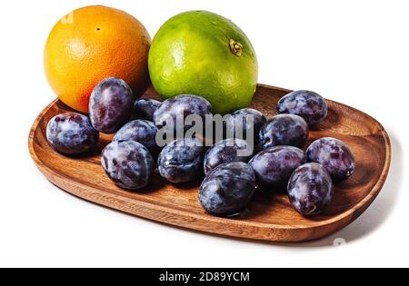 Fruits of pink and green grapefruit with plum on a wooden platter isolated on white background. Summer fruits composition. Stock Photo