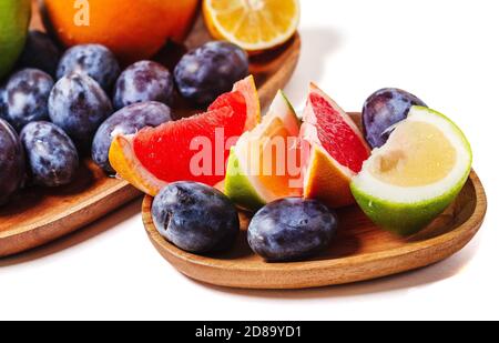 Slices of grapefruit and plum on a wooden dish close up isolated on a white background. Fresh summer fruits composition. Stock Photo