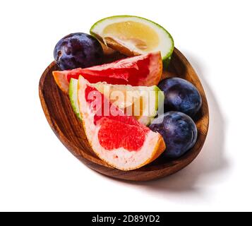 Slices of grapefruit and plum on a wooden dish close up isolated on a white background. Fresh summer fruits composition. Stock Photo