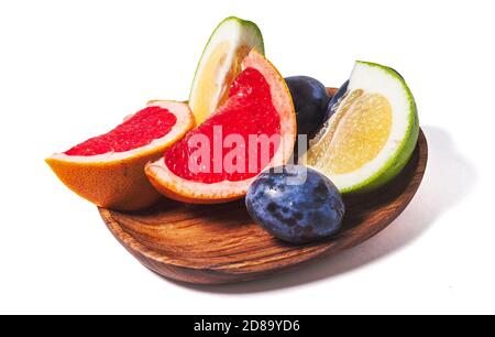 Slices of grapefruit and plum on a wooden plate close up isolated on a white background. Fresh summer fruits composition. Stock Photo