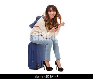 Full body portrait of young travel woman sitting on suitcase with mobile phone Stock Photo
