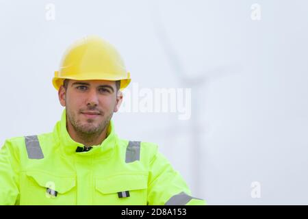 Portrait of smiling young engineer in front of blurred wind turbines in the background Stock Photo