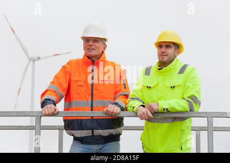 Smiling young and mature engineers in front of blurred wind turbine in the background Stock Photo
