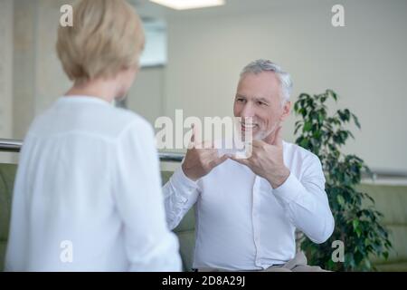 Bearded gray-haired man talking with blonde woman using sign language Stock Photo
