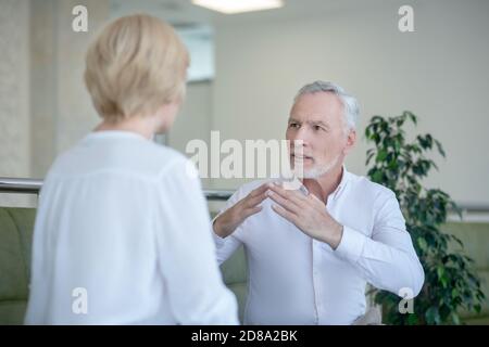 Bearded gray-haired man and blonde woman talking using sign language Stock Photo