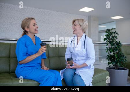 Two female medical workers sitting on sofa, enjoying coffee Stock Photo