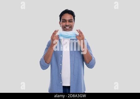 Indian Man Puts on Medical Mask Isolated. Man In Blue Shirt Showing How to put on Medical Mask. Health, Virus, Medical Concept Stock Photo