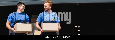 Panoramic orientation of movers holding cardboard boxes and looking at each other on urban street Stock Photo