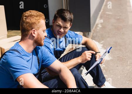 Loaders with pen and clipboard talking while sitting in warehouse outdoors Stock Photo