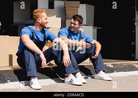 Movers talking while sitting in warehouse outdoors Stock Photo