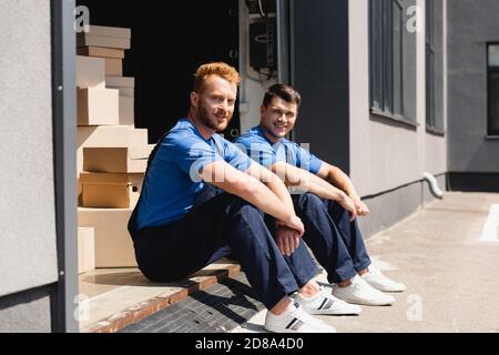 Selective focus of loaders looking at camera while sitting in warehouse outdoors Stock Photo