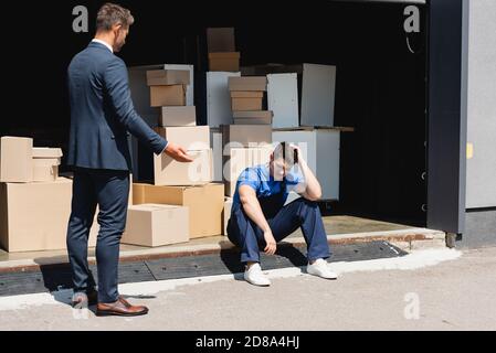 Businessman pointing with hand near upset loader in warehouse outdoors Stock Photo