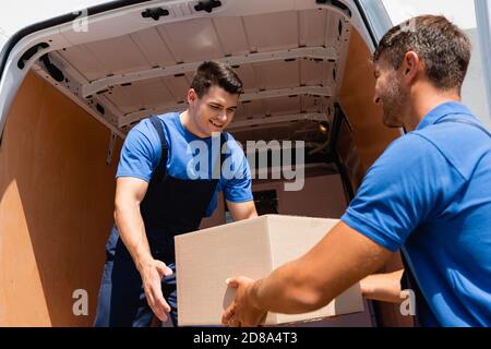 Movers with cardboard box unloading truck on urban street Stock Photo