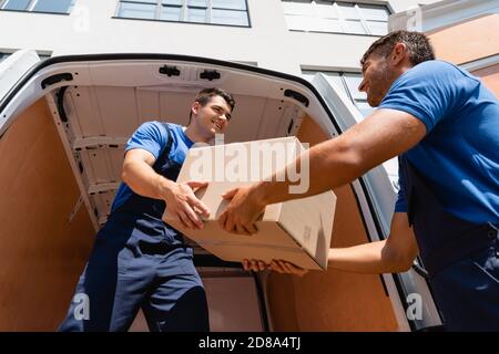Low angle view of loaders looking at each other while holding cardboard box in truck on urban street Stock Photo
