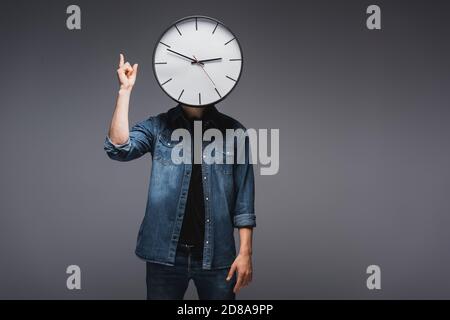 Man with clock near face pointing with fingers on grey background, concept of time management