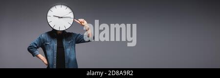 Panoramic orientation of man pointing with finger at clock on head on grey background, concept of time management