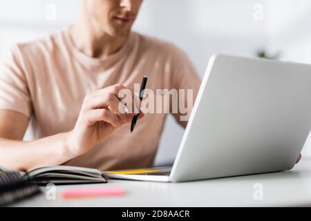 Cropped view of freelancer holding pen and using laptop on table, earning online concept Stock Photo