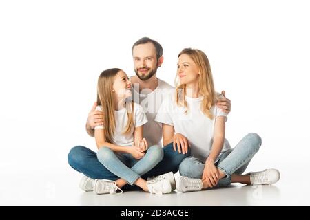 happy family sitting on floor with crossed legs and embracing isolated on white Stock Photo