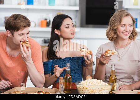 joyful multicultural friends eating pizza near bowl of popcorn Stock Photo