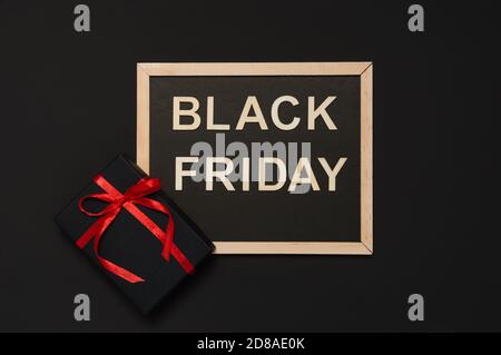 Black Friday sale concept. Black gift with red ribbon bow and blackboard with words from wooden letters on dark background. Flat lay style, top view Stock Photo