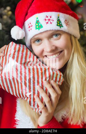 Christmas portrait of happy young woman holding a wrapped gift/present wearing red Santa hat.