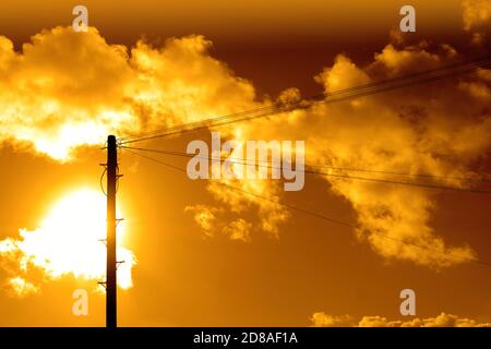 Power telephone post and lines against large sun and cumulus cloud and golden sky Stock Photo