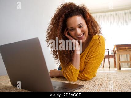 Portrait of happy african american woman lying on floor looking at laptop computer Stock Photo