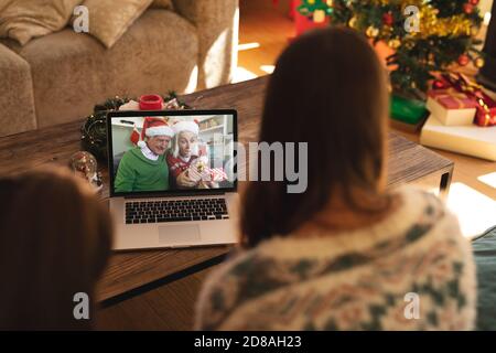 Rear view of woman and son having a videocall with senior couple in santa hats opening gift box on l Stock Photo