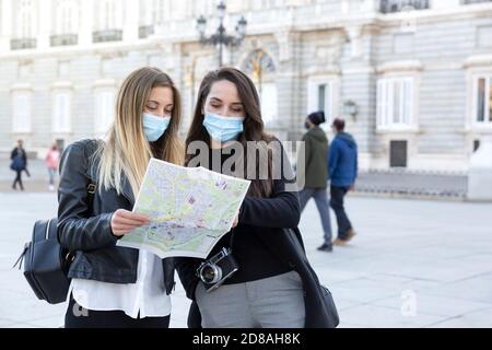 Two girls looking at a tourist map on the street. They are wearing face masks. Concept of travel during the Covid-19 pandemic. Stock Photo