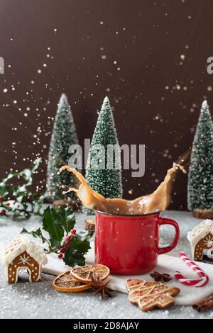 Splashes of Christmas cappuccino in red mug on grey table with gingerbread cookies and other Christmas decorations. Merry Christmas greeting card. Stock Photo