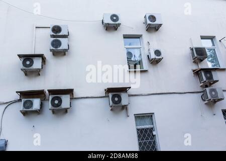 Air conditioners on the wall of the house where the offices are located. White plaster and enclosures of the external units of the ventilation system. Stock Photo