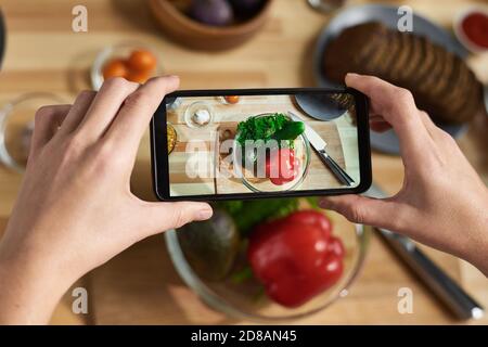 Close-up of female hands holding mobile phone and making photo of fresh vegetables in bowl Stock Photo