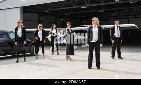 Famous female celebrity with bodyguards surrounded. VIP security agents and close protection officers Stock Photo