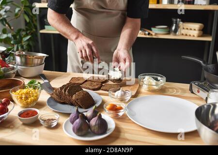 Close-up of chef in apron putting butter on bread he preparing toasters at the table in the kitchen Stock Photo