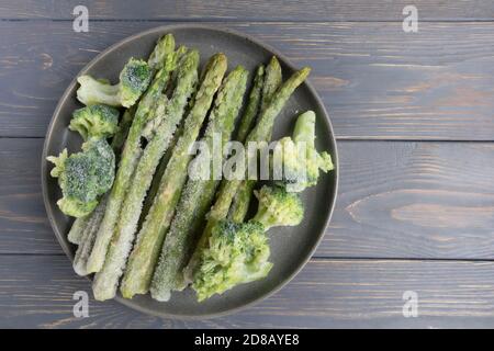 Frozen asparagus and broccoli in a plate on a wooden surface with space for text. Article, recipe. Stock Photo