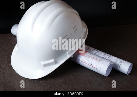 White hardhat and rolled engineering drawings at engineer workplace Stock Photo
