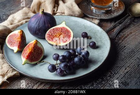 Whole and cut figs and blue grapes in a plate on a wooden table Stock Photo