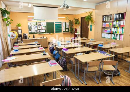 Saint-Petersburg, Russia, circa Sep, 2017: Russian schoolclass with many pupil desks, teacher table and green blackboard. School bags and textbooks ar Stock Photo