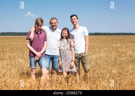 Single father with his teenage children, two sons and daughter. Cereal farmer family standing on wheat fields, embracing and loving people Stock Photo
