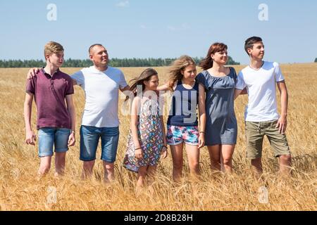 Family with many teenage children embracing together while standing on golden wheat fields, smiling people Stock Photo