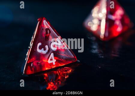 Close up of two red 4 sided dice on a wet slate surface. Focused on the front. Lens flare Stock Photo