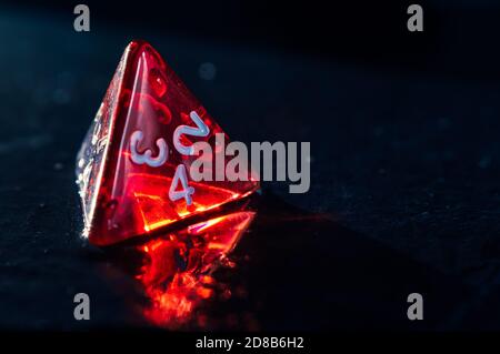 Close up of one red 4 sided dice with little water drops  on a wet slate surface. Stock Photo