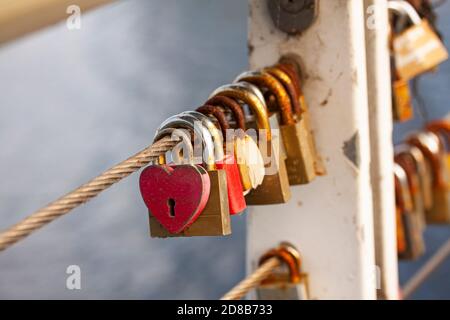Symbolic love padlocks fixed to a railing wire on a bridge. The first one i red and heart shaped. Selective focus with shallow depth of field. Stock Photo