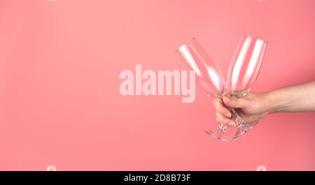 A woman holds two champagne glasses in her hand on a soft pink background. Stock Photo